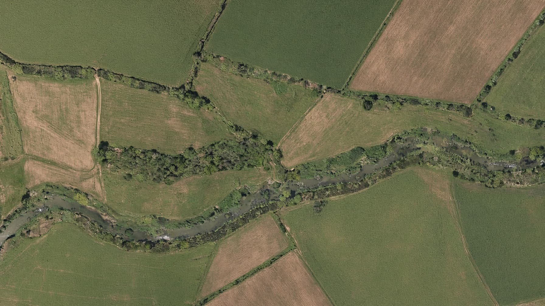 Top-down orthomosaic-style aerial of fields and a creek
